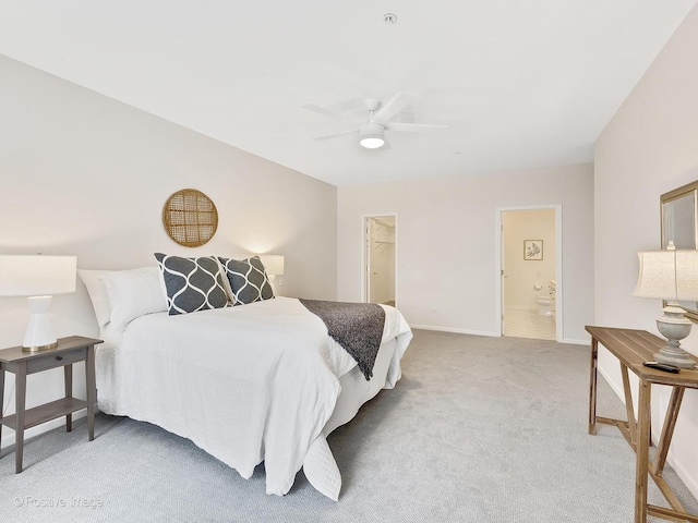 bedroom featuring baseboards, light colored carpet, ceiling fan, ensuite bathroom, and a walk in closet