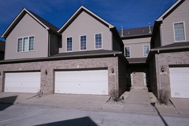 view of property with a garage, brick siding, and driveway