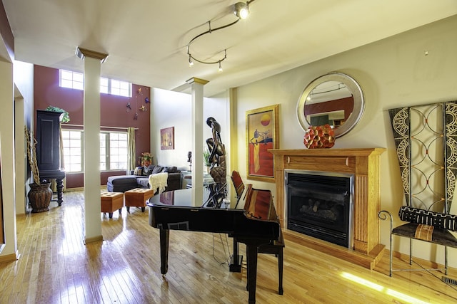 living area featuring baseboards, light wood-style floors, a fireplace, and ornate columns