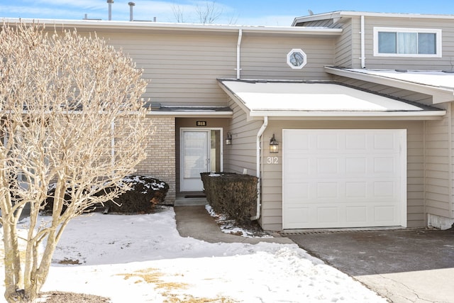 snow covered property entrance featuring a garage and brick siding