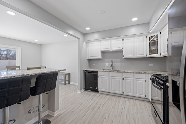 kitchen featuring a breakfast bar, a sink, white cabinets, black appliances, and light wood finished floors