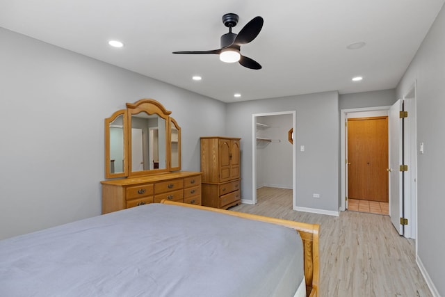 bedroom featuring a walk in closet, recessed lighting, light wood-style floors, a ceiling fan, and baseboards