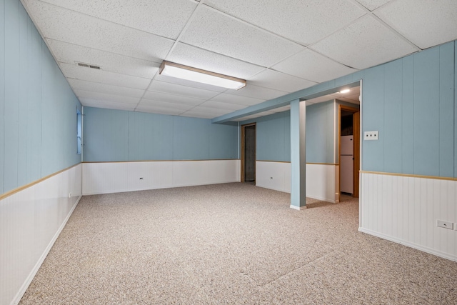 finished basement featuring visible vents, a paneled ceiling, carpet flooring, and freestanding refrigerator