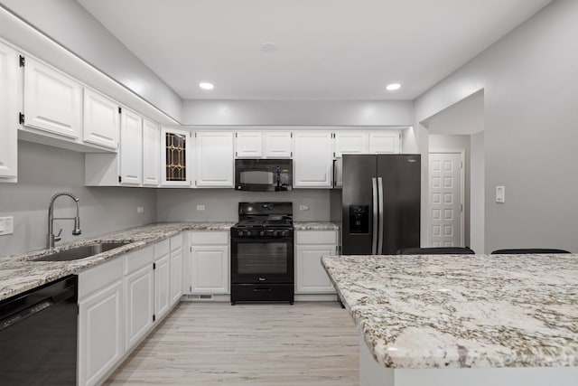 kitchen featuring light wood-type flooring, black appliances, white cabinets, and a sink