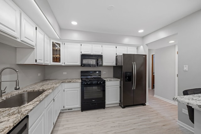 kitchen with a sink, white cabinets, light stone countertops, black appliances, and glass insert cabinets