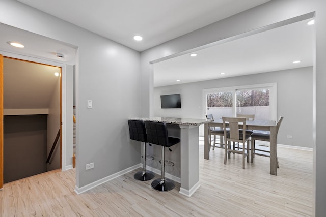 kitchen featuring a peninsula, a breakfast bar, light wood-style flooring, and baseboards