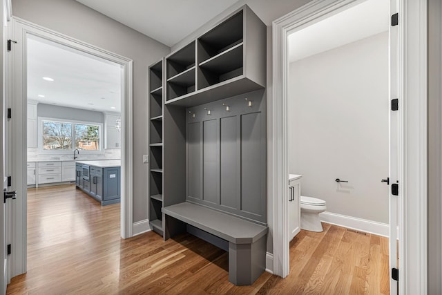 mudroom with light wood-type flooring, a sink, and baseboards
