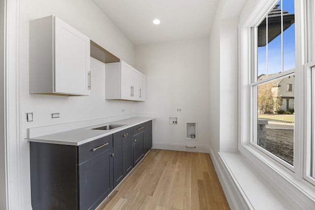 laundry area with light wood-style flooring, washer hookup, a sink, baseboards, and cabinet space