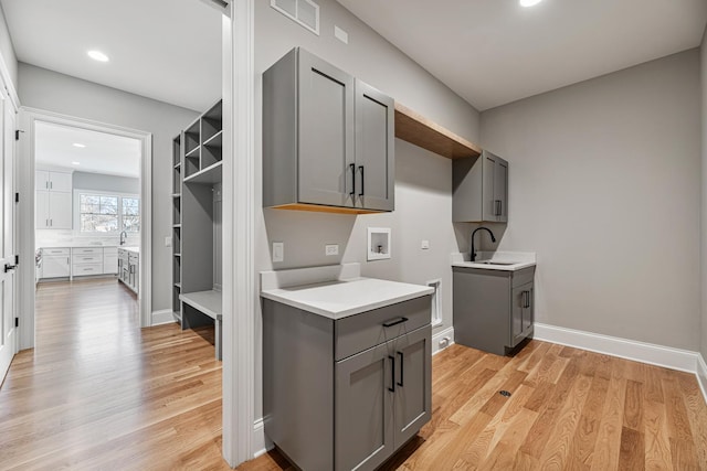 kitchen with light wood-style flooring, a sink, light countertops, gray cabinets, and open shelves