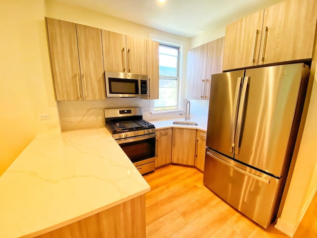 kitchen with a peninsula, a sink, appliances with stainless steel finishes, light wood-type flooring, and light stone countertops