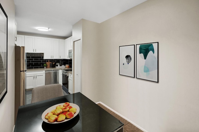 kitchen with baseboards, decorative backsplash, stainless steel appliances, dark tile patterned floors, and white cabinetry