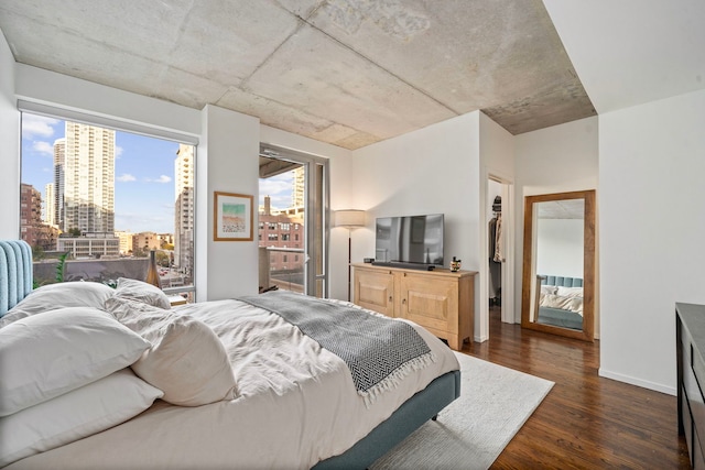 bedroom with dark wood-style floors, a view of city, baseboards, and a walk in closet