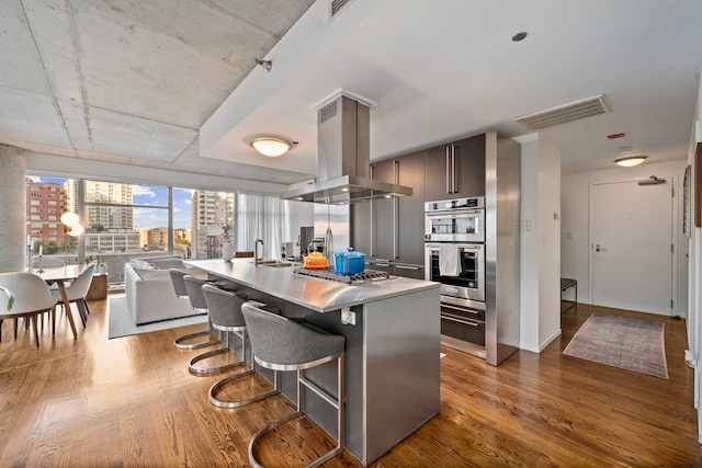 kitchen with island range hood, visible vents, a view of city, modern cabinets, and a kitchen bar