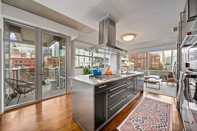 kitchen featuring island range hood, a center island, dark cabinetry, a city view, and a sink