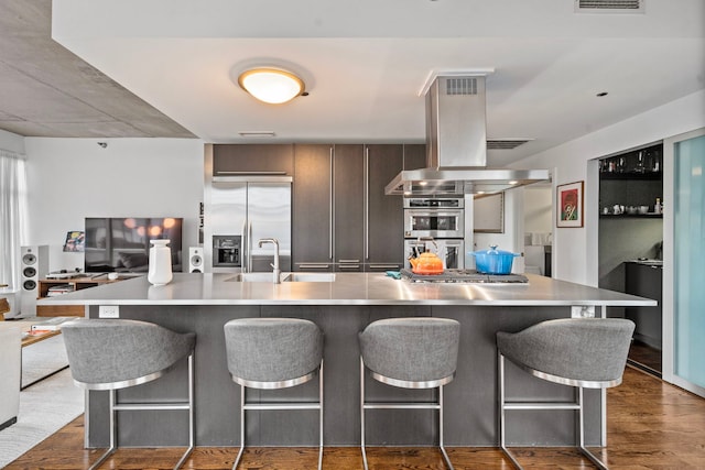 kitchen featuring island exhaust hood, light countertops, appliances with stainless steel finishes, a sink, and modern cabinets