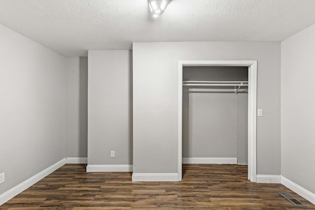 unfurnished bedroom with a closet, dark wood finished floors, visible vents, and baseboards