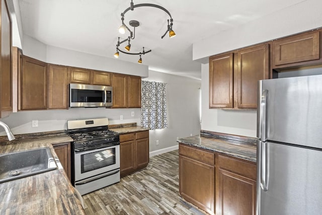 kitchen featuring wood finished floors, a sink, baseboards, appliances with stainless steel finishes, and brown cabinets