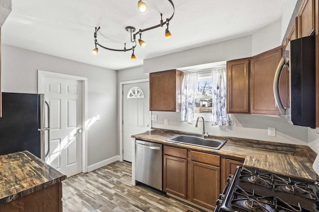 kitchen featuring light wood finished floors, stainless steel appliances, a sink, butcher block countertops, and baseboards