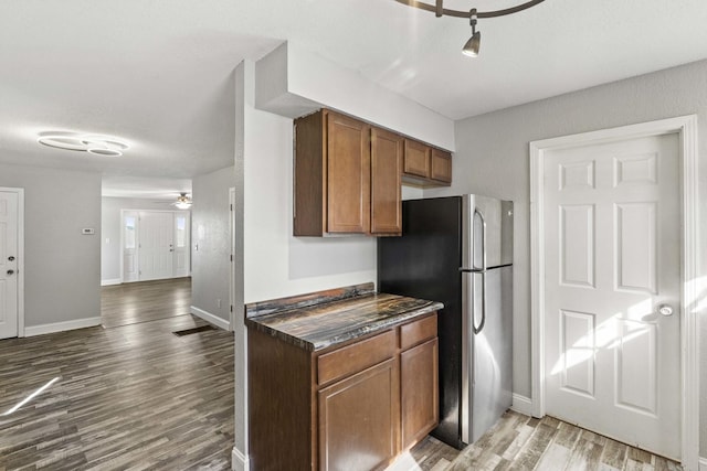 kitchen with brown cabinets, dark countertops, freestanding refrigerator, wood finished floors, and baseboards