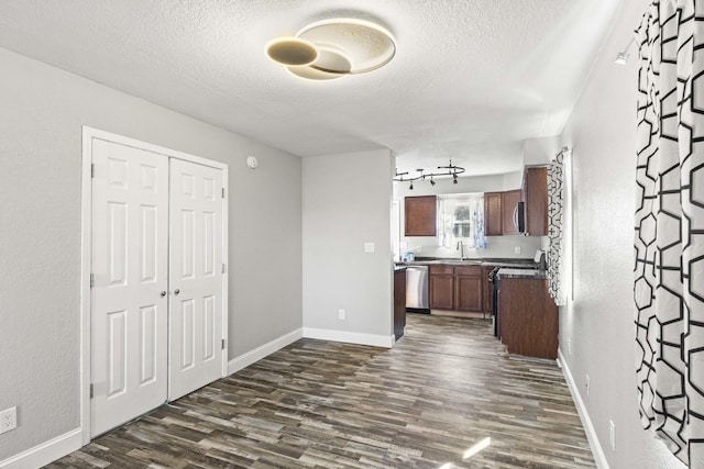 kitchen with dark wood-style floors, stainless steel appliances, dark countertops, a sink, and a textured ceiling