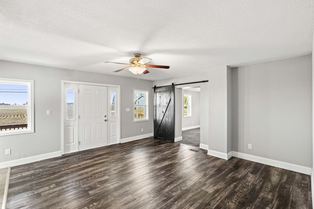 entrance foyer featuring a barn door, baseboards, a ceiling fan, dark wood-style flooring, and a textured ceiling