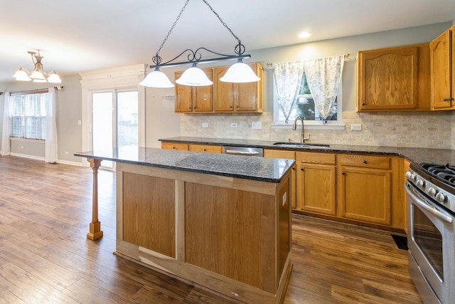 kitchen featuring stainless steel appliances, a sink, a center island, dark stone counters, and dark wood finished floors