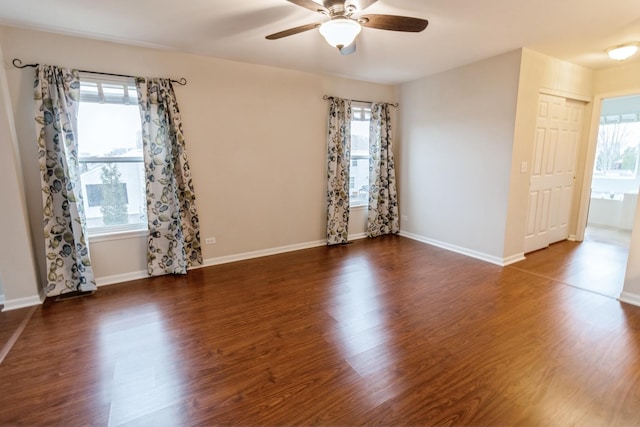 empty room with a ceiling fan, baseboards, and dark wood-type flooring