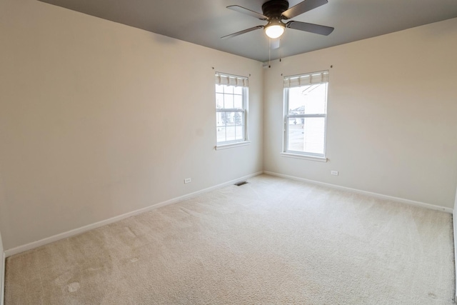 spare room with a ceiling fan, light carpet, visible vents, and baseboards