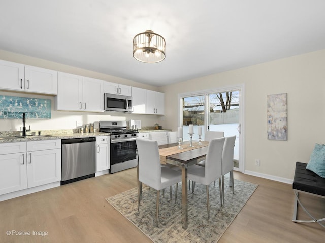 kitchen featuring light stone counters, stainless steel appliances, a sink, white cabinetry, and light wood-style floors