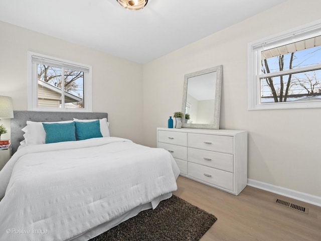 bedroom with light wood-type flooring, baseboards, multiple windows, and visible vents