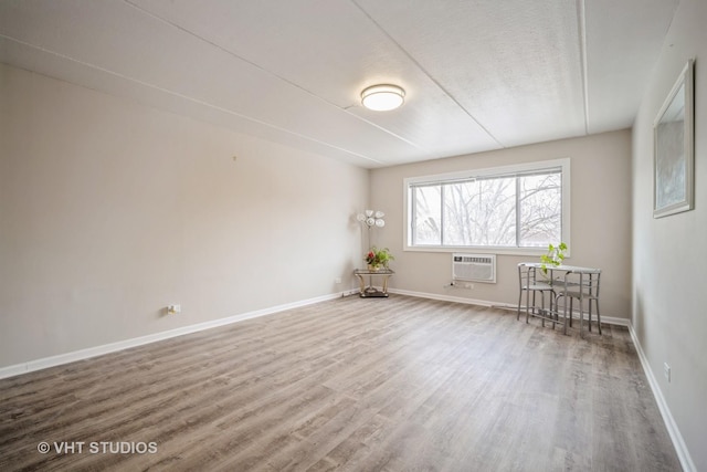 unfurnished room with a textured ceiling, an AC wall unit, wood finished floors, and baseboards