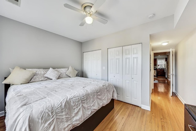 bedroom with baseboards, visible vents, a ceiling fan, wood finished floors, and multiple closets