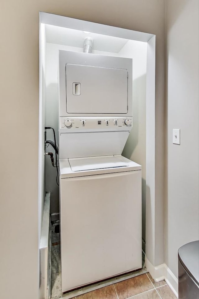 washroom with stacked washer / drying machine, laundry area, baseboards, and light tile patterned floors