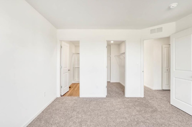 unfurnished bedroom featuring a walk in closet, a closet, visible vents, light carpet, and baseboards