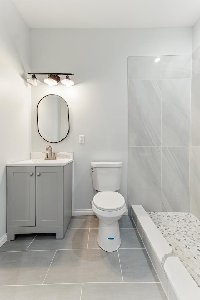 bathroom with vanity, baseboards, tiled shower, tile patterned floors, and toilet