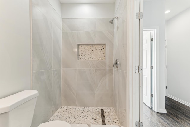 bathroom featuring toilet, wood finished floors, baseboards, and tiled shower