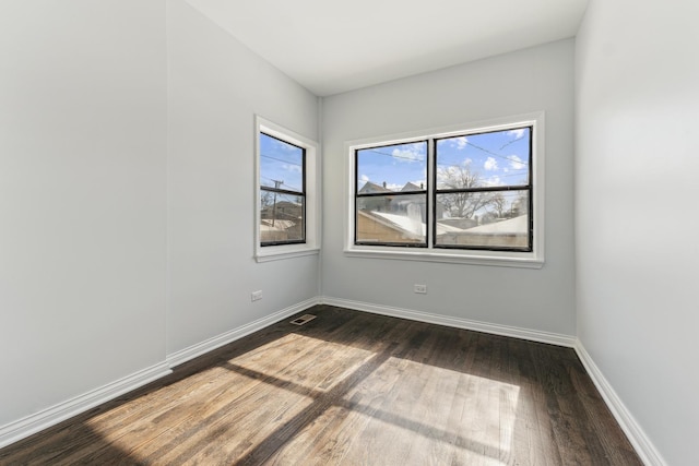 spare room featuring visible vents, baseboards, and dark wood-style flooring