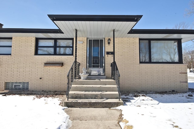 snow covered property entrance featuring brick siding and crawl space