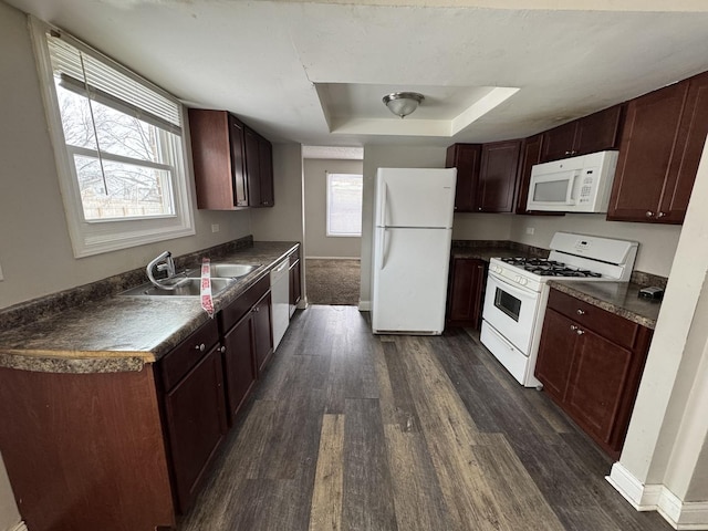 kitchen featuring white appliances, dark countertops, dark wood-type flooring, a tray ceiling, and a wealth of natural light