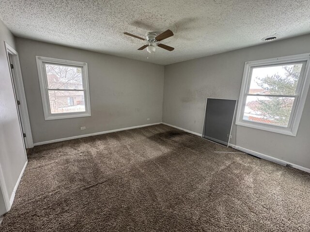 empty room featuring dark colored carpet, visible vents, a textured ceiling, and baseboards