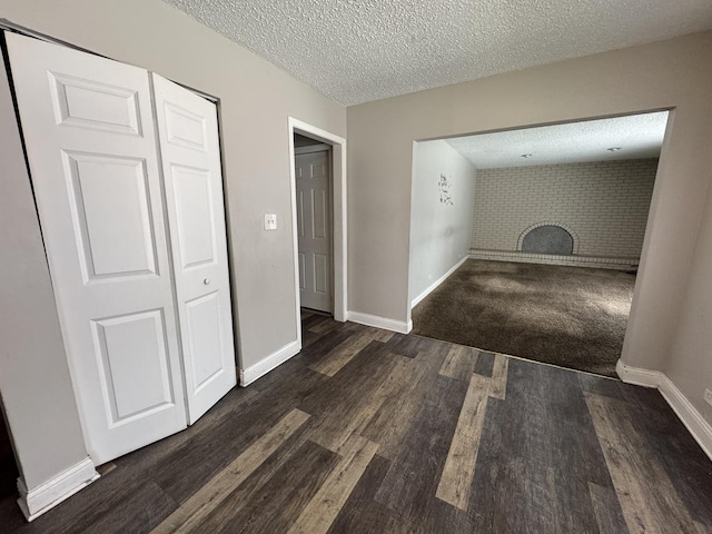 interior space with a textured ceiling, a fireplace, baseboards, and dark wood-style flooring