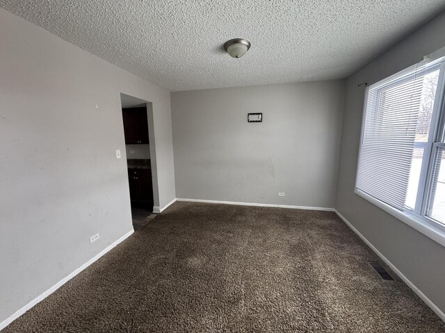 unfurnished room featuring visible vents, baseboards, dark colored carpet, and a textured ceiling