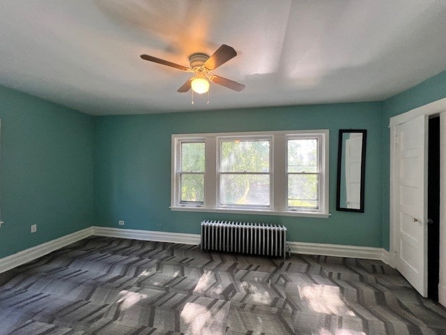 spare room with baseboards, ceiling fan, and radiator