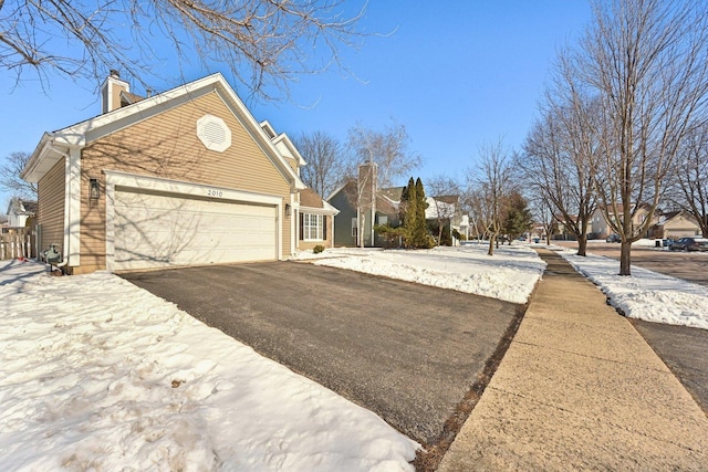 view of snowy exterior with aphalt driveway, a chimney, an attached garage, and a residential view