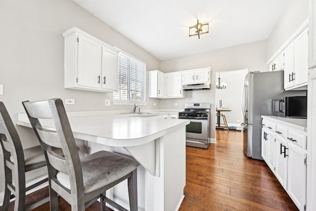 kitchen featuring under cabinet range hood, stainless steel appliances, a peninsula, light countertops, and dark wood finished floors