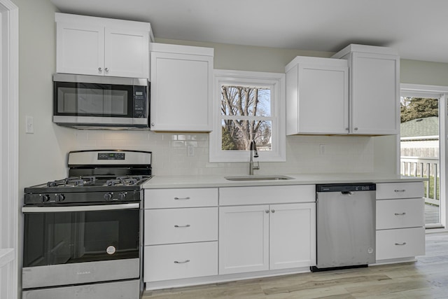 kitchen with light countertops, appliances with stainless steel finishes, white cabinets, a sink, and plenty of natural light