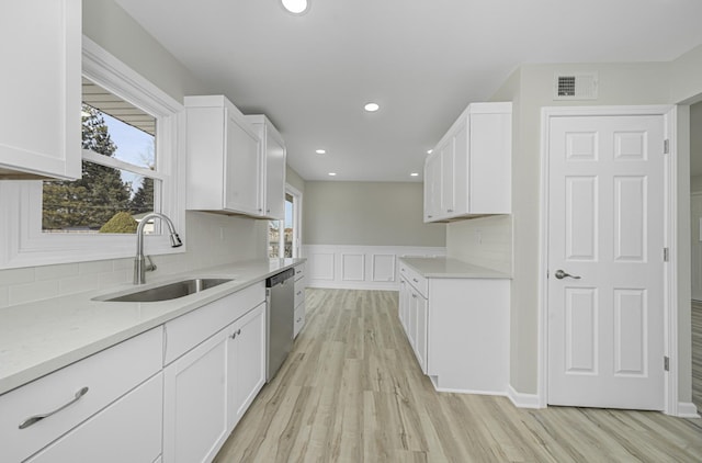 kitchen with light wood-style flooring, a sink, white cabinetry, backsplash, and dishwasher