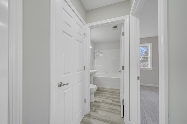 bathroom featuring baseboards, visible vents, toilet, wood finished floors, and shower / bathing tub combination