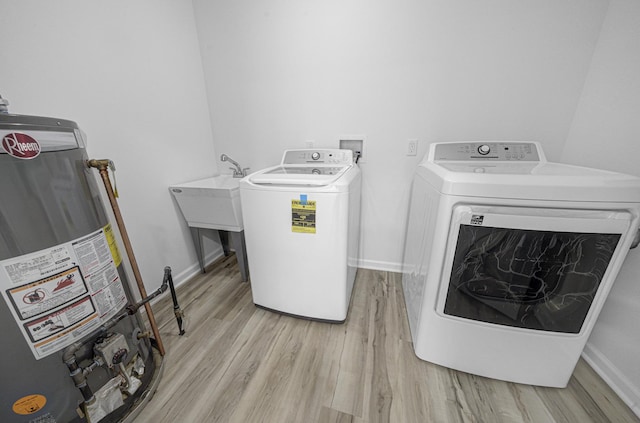 clothes washing area with light wood-style flooring, laundry area, baseboards, water heater, and washer and clothes dryer