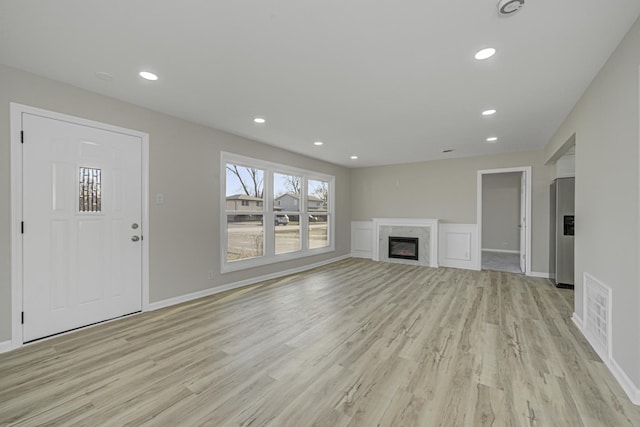 unfurnished living room with light wood-style flooring, recessed lighting, a premium fireplace, visible vents, and baseboards